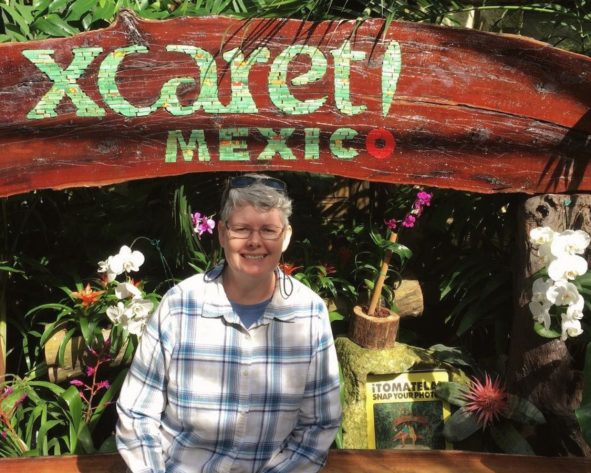 Dee is sitting under a sign during a quiet visit while travelling, reflecting a slower, more thoughtful way of exploring.
