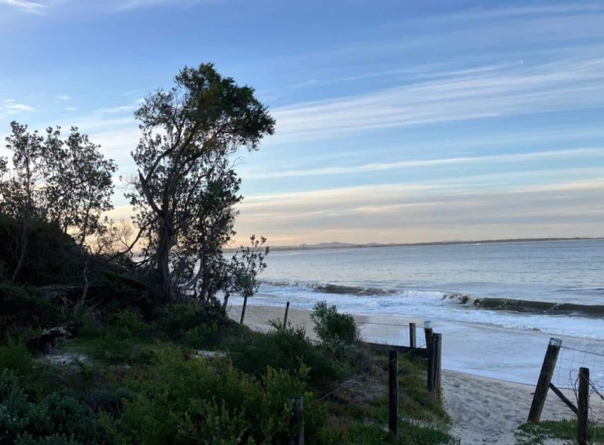 A quiet beach with gentle waves, coastal trees, and a soft blue sky in the early morning or evening. This peaceful nearby outing reflects local travel ideas for retirees who want to begin exploring again without going far from home.